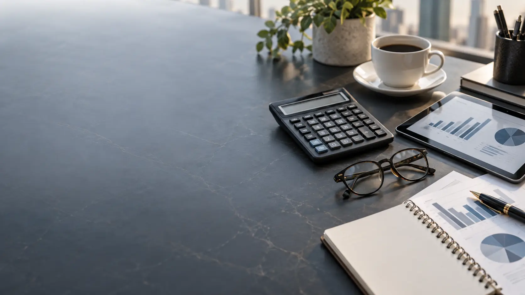 Calculator, glasses and a tablet showing financial charts on a dark desk
